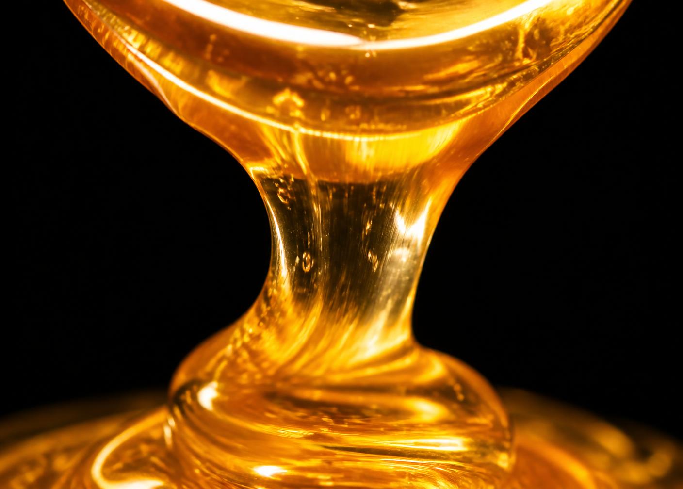 Close-up of thick golden Nyuki Gold honey pouring against a black background